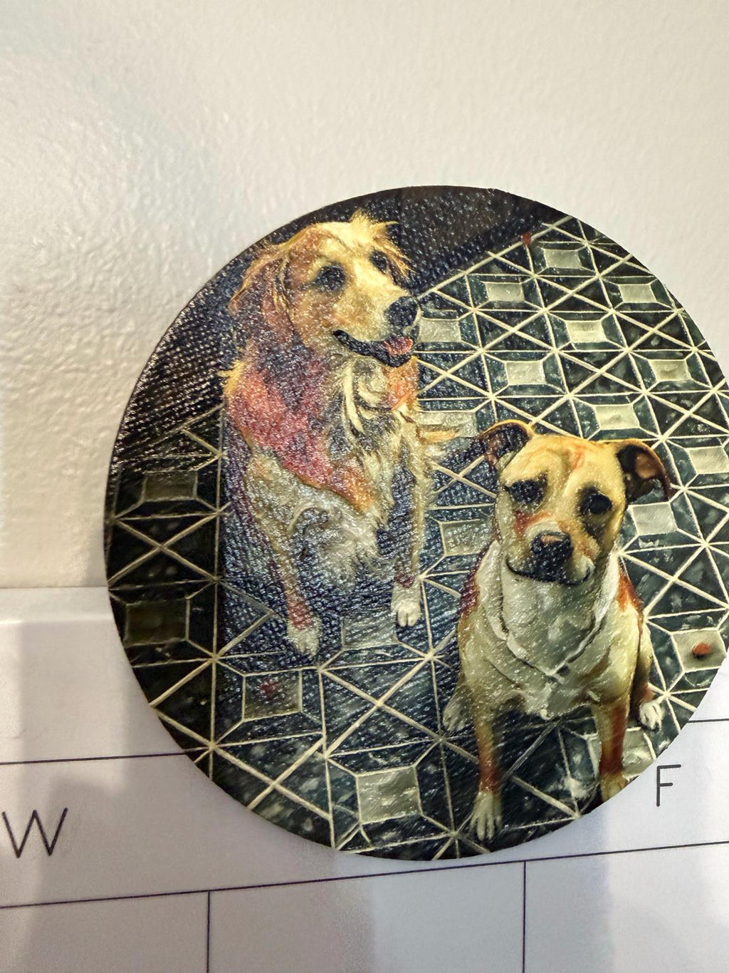 Custom Pet Portrait Magnet with a textured brushstroke portrait of two dogs on a geometric dark pattern, shown against a white wall above a calendar page
