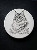 maine coon cat line art ceramic coaster cat lover gift idea pet portrait drink coaster housewarming gift cat mom home decor kitchen barware with a detailed black ink maine coon portrait and botanical floral accents on a round white tile, shown on a dark slate surface