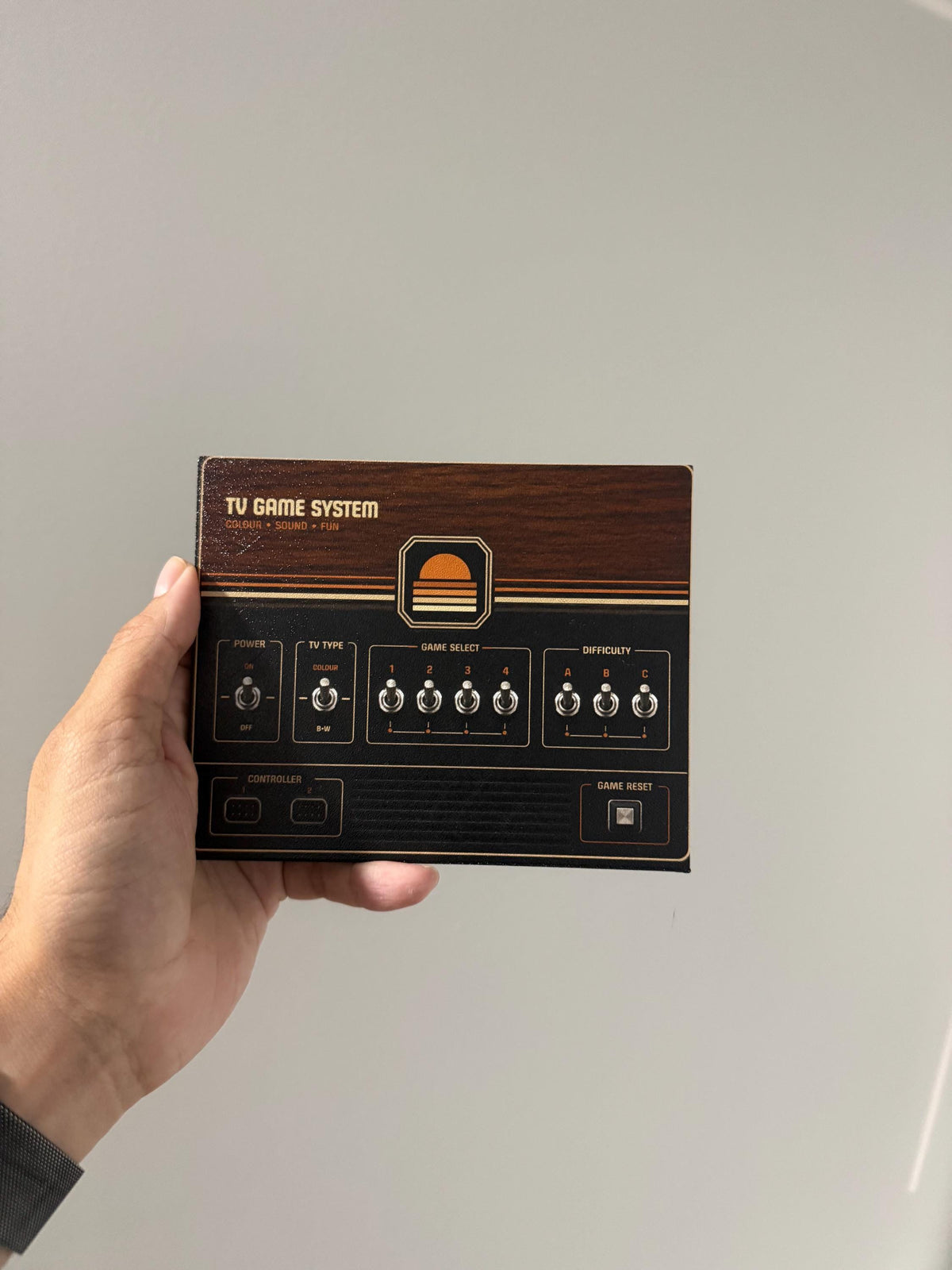 Retro Woodgrain Steam Machine Faceplate – 70s Atari Inspired Console Cover, hand holding the uninstalled woodgrain faceplate panel against a plain light gray wall