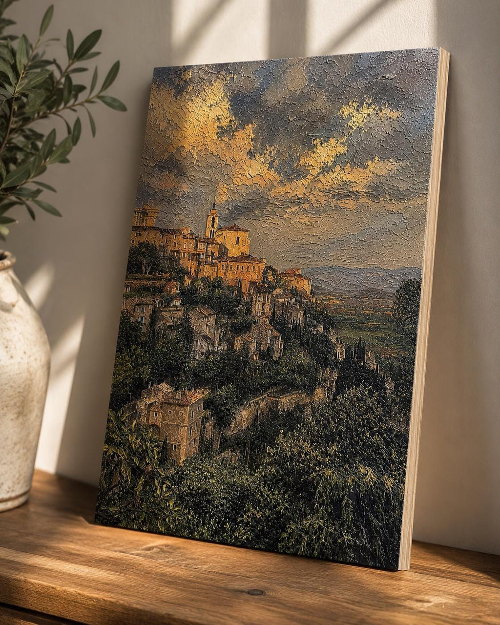 Tuscany Hill Town Textured Painting Print canvas leaning against a beige wall on a wooden surface beside a potted plant, with the hillside village artwork lit by natural window light