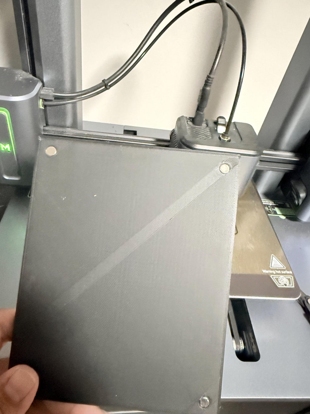 Synthwave Steam Machine Faceplate UV Printed Front Panel | Retro Neon Sunset Grid Art | Custom Mini PC Cover | Gamer Gift, hand holding the unprinted black faceplate panel in front of a 3D printer, showing the panel's back side with its diagonal design