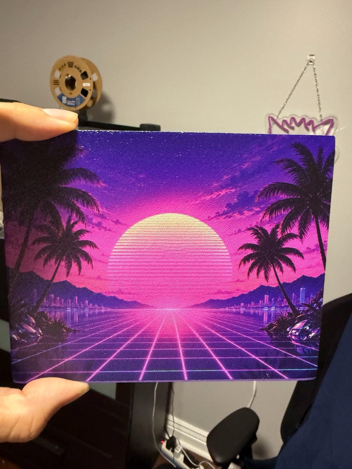 Synthwave Steam Machine Faceplate UV Printed Front Panel | Retro Neon Sunset Grid Art | Custom Mini PC Cover | Gamer Gift, hand holding the uninstalled synthwave faceplate panel, with a 3D printer filament spool in the background