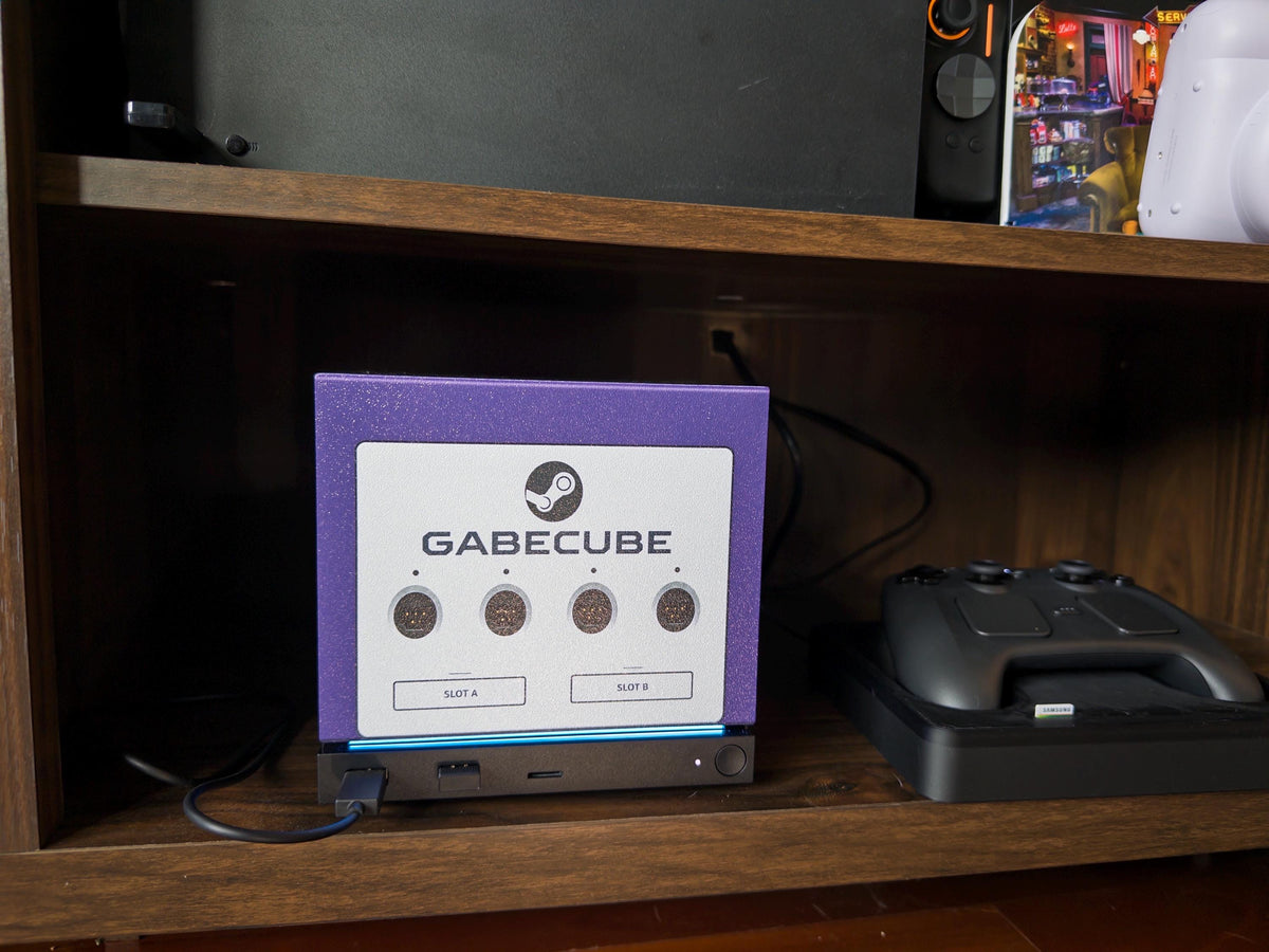 3D Printed GameCube Faceplate – Indigo Purple Steam Machine Controller Panel, angled close-up of the GabeCube indigo purple faceplate installed on the console on a wooden shelf beside a Steam controller on its dock