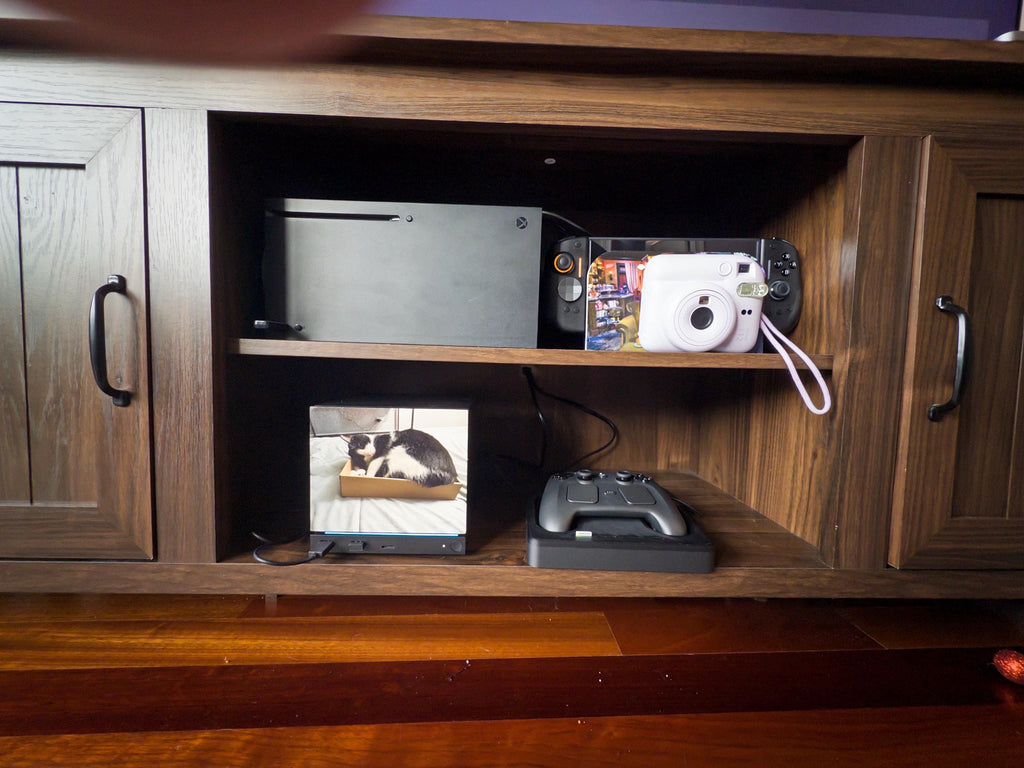 Custom Steam Machine Faceplate, Build your own Personalized Magnetic Cover Plate, Your Photo or Art UV Printed, Gamer Gift Valve Steam, wooden entertainment cabinet with a Steam Deck with a colorful custom faceplate installed on the top shelf beside an Xbox and a white instant camera, with a cat photo frame and Steam controller on the lower shelf
