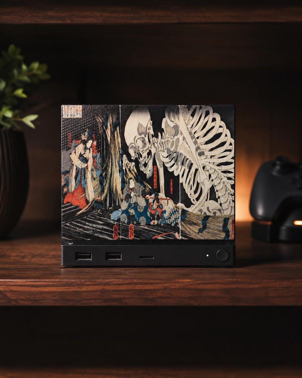 Steam Machine Faceplate, Kuniyoshi Ukiyo-e Skeleton Art, UV Printed Panel with the colossal skeleton ukiyo-e artwork, straight-on front view installed on the console on a dark wooden shelf with a plant and a game controller