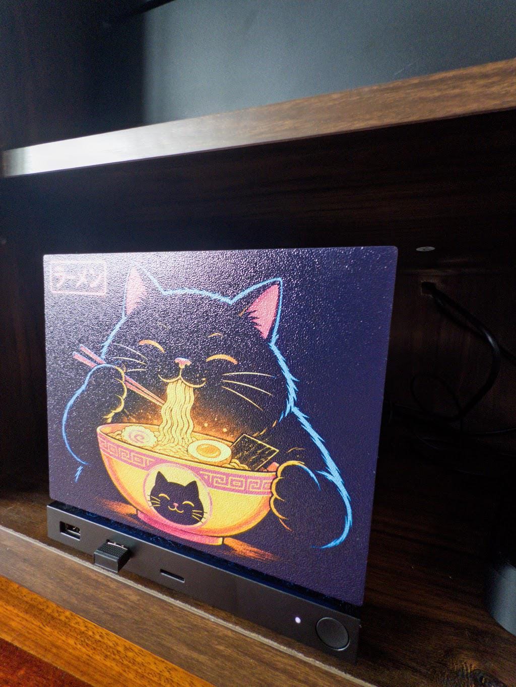 Steam Machine Faceplate Neon Ramen Cat Art | Magnetic UV Printed Panel | Kawaii Japanese Gamer Decor, angled close-up of the Neon Ramen Cat faceplate installed on the console on a wooden shelf, showing the full black cat eating ramen artwork with the glowing neon ramen sign