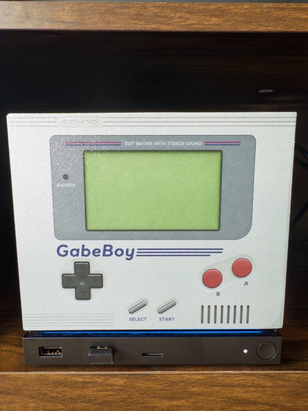 GabeBoy Retro Handheld Style Steam Machine Faceplate, close-up straight-on view of the console on a dark wooden surface showing the green screen, gray D-pad and red buttons