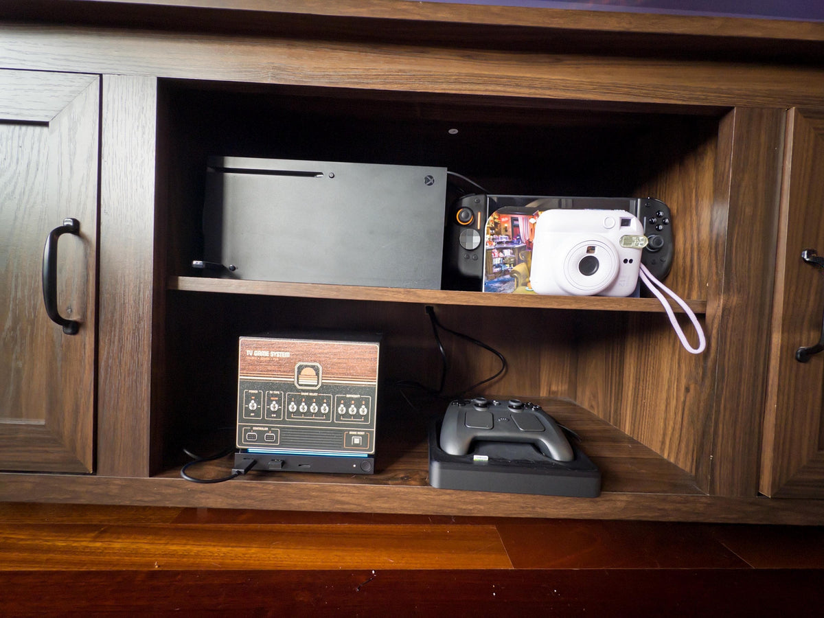 Custom Steam Machine Faceplate, Build your own Personalized Magnetic Cover Plate, Your Photo or Art UV Printed, Gamer Gift Valve Steam, retro woodgrain sample faceplate installed on the Steam Machine on the lower shelf of a wooden entertainment cabinet, with a Steam controller on its charging dock beside it and an Xbox, Steam Deck and instant camera on the upper shelf