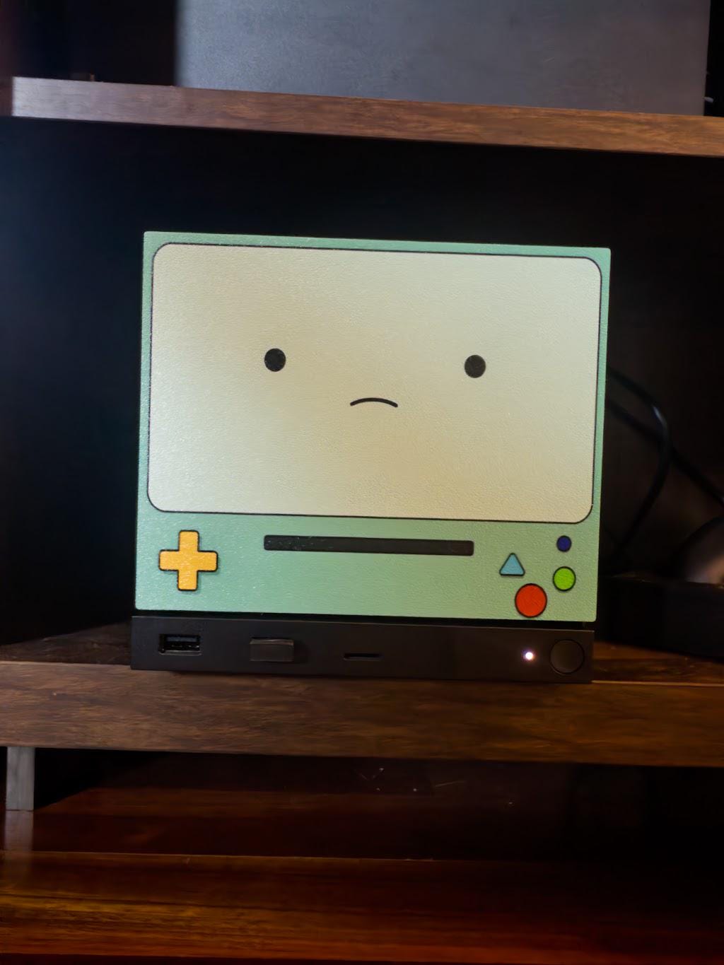 Robot Face Console Skin 2-Pack, Happy Sad Expression, Kawaii Gaming Setup Upgrade, sad expression skin shown installed on the console in a close-up front view on a dark wooden shelf