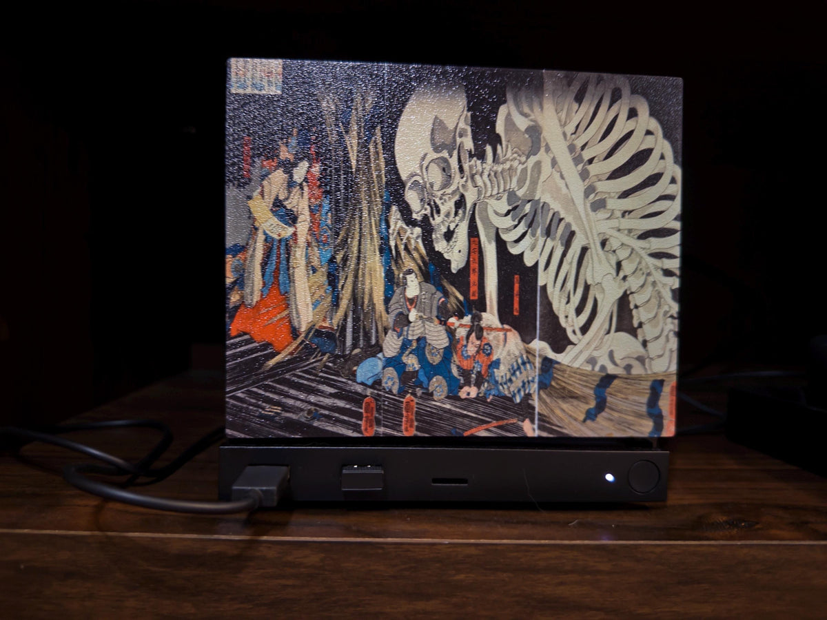 Steam Machine Faceplate, Kuniyoshi Ukiyo-e Skeleton Art, UV Printed Panel with the giant skeleton ukiyo-e artwork, straight-on view installed on the console on a dark wooden surface against a black background with a power cable connected