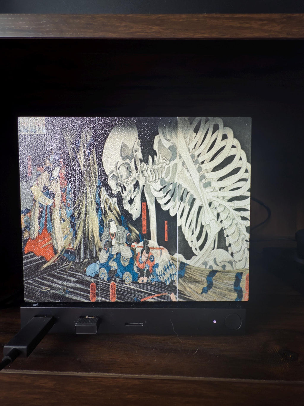 Steam Machine Faceplate, Kuniyoshi Ukiyo-e Skeleton Art, UV Printed Panel with the giant skeleton ukiyo-e artwork, front view installed on the console on a dark wooden surface against a black background with a power cable to the left