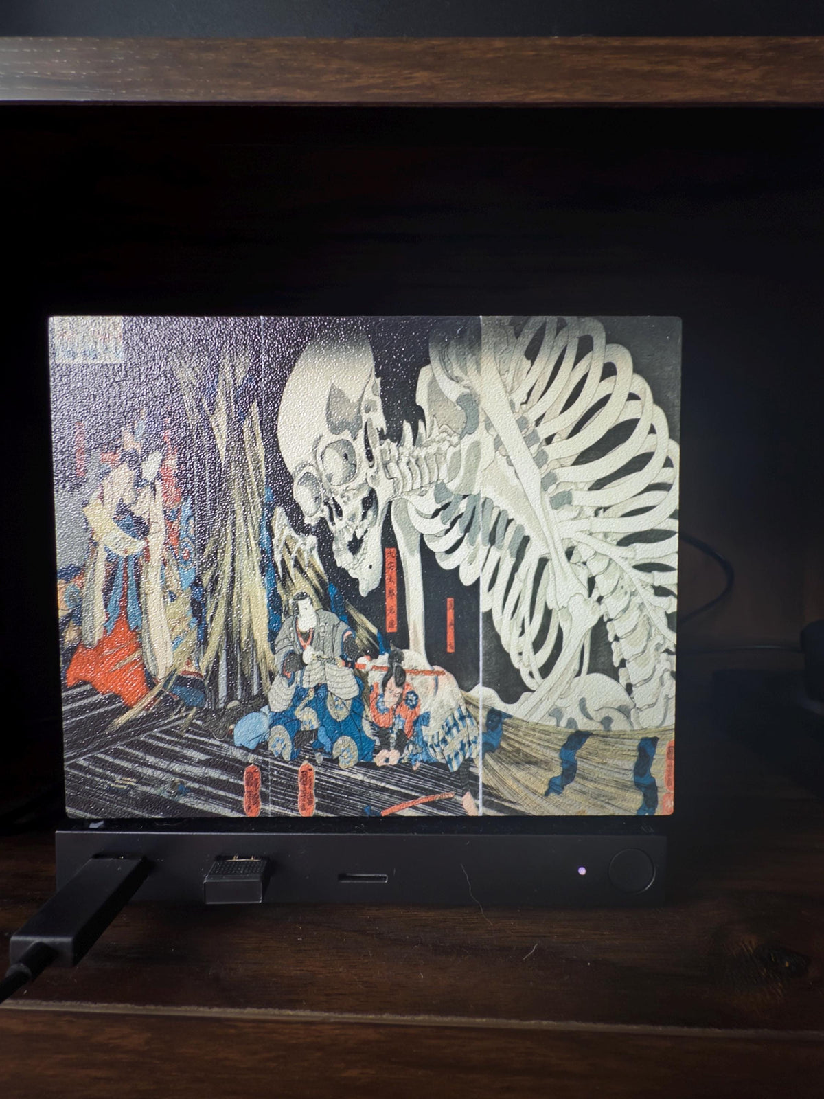 Steam Machine Faceplate, Kuniyoshi Ukiyo-e Skeleton Art, UV Printed Panel with the giant skeleton ukiyo-e artwork, front view installed on the console on a dark wooden surface against a black background with a power cable to the left
