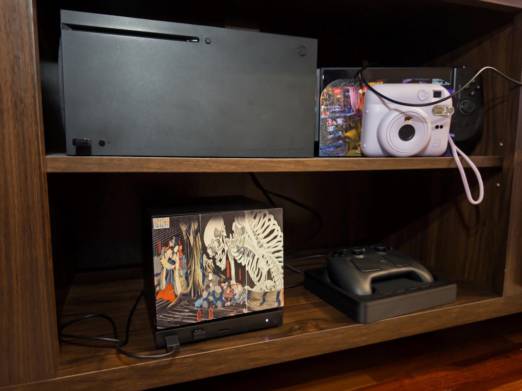 Steam Machine Faceplate, Kuniyoshi Ukiyo-e Skeleton Art, UV Printed Panel with the giant skeleton ukiyo-e artwork, shown installed on the console on the lower shelf of a wooden media cabinet beside a game controller