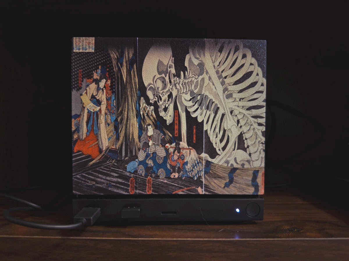 Steam Machine Faceplate, Kuniyoshi Ukiyo-e Skeleton Art, UV Printed Panel with the colossal skeleton ukiyo-e artwork, close-up straight-on view installed on the console against a dark background with a power cable connected