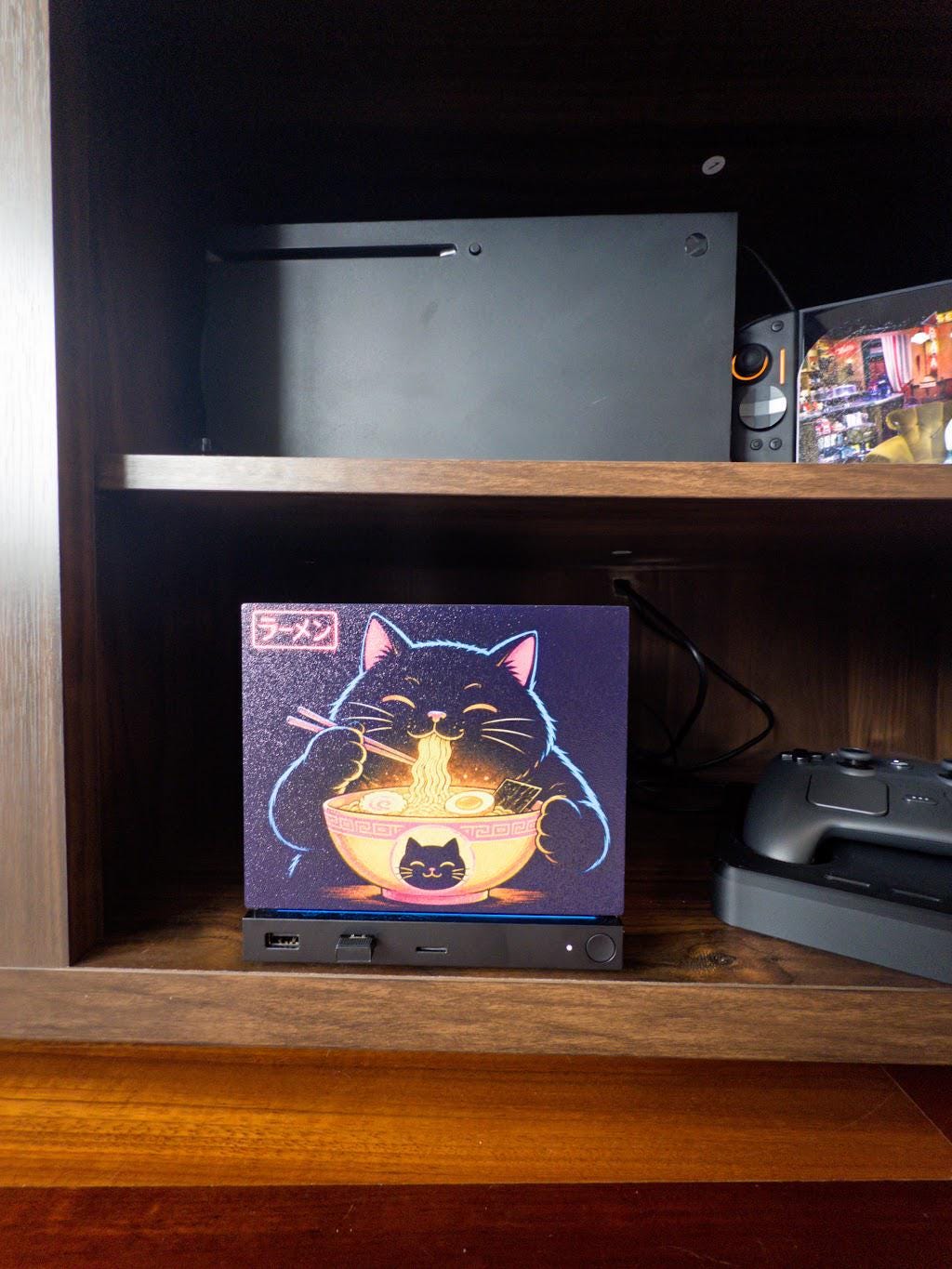 Steam Machine Faceplate Neon Ramen Cat Art | Magnetic UV Printed Panel | Kawaii Japanese Gamer Decor, Neon Ramen Cat faceplate installed on the console on a wooden shelf, with a game console on the shelf above and a Steam controller beside it