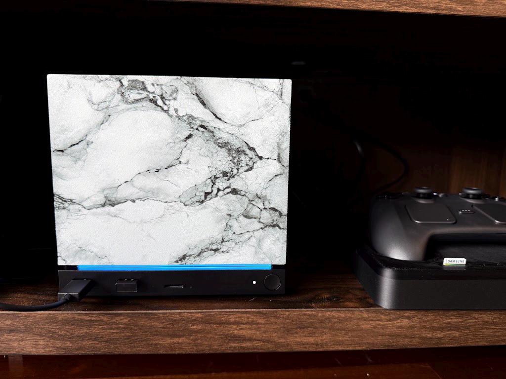 White Marble Steam Machine Faceplate | Magnetic UV Printed Panel, Minimal Desk Decor, front view of the console with the white marble faceplate installed on a dark wooden shelf, with a black Steam controller on its charging dock beside it
