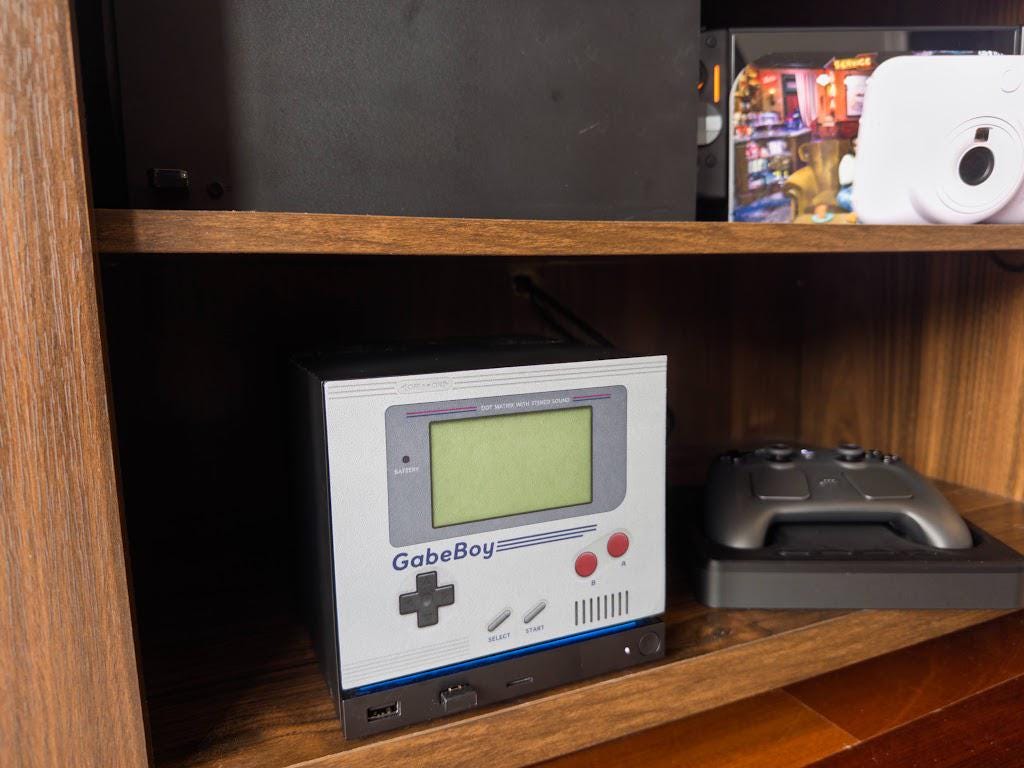 GabeBoy Retro Handheld Style Steam Machine Faceplate on the console, shown on a wooden shelf next to a game controller in a three-quarter angle view