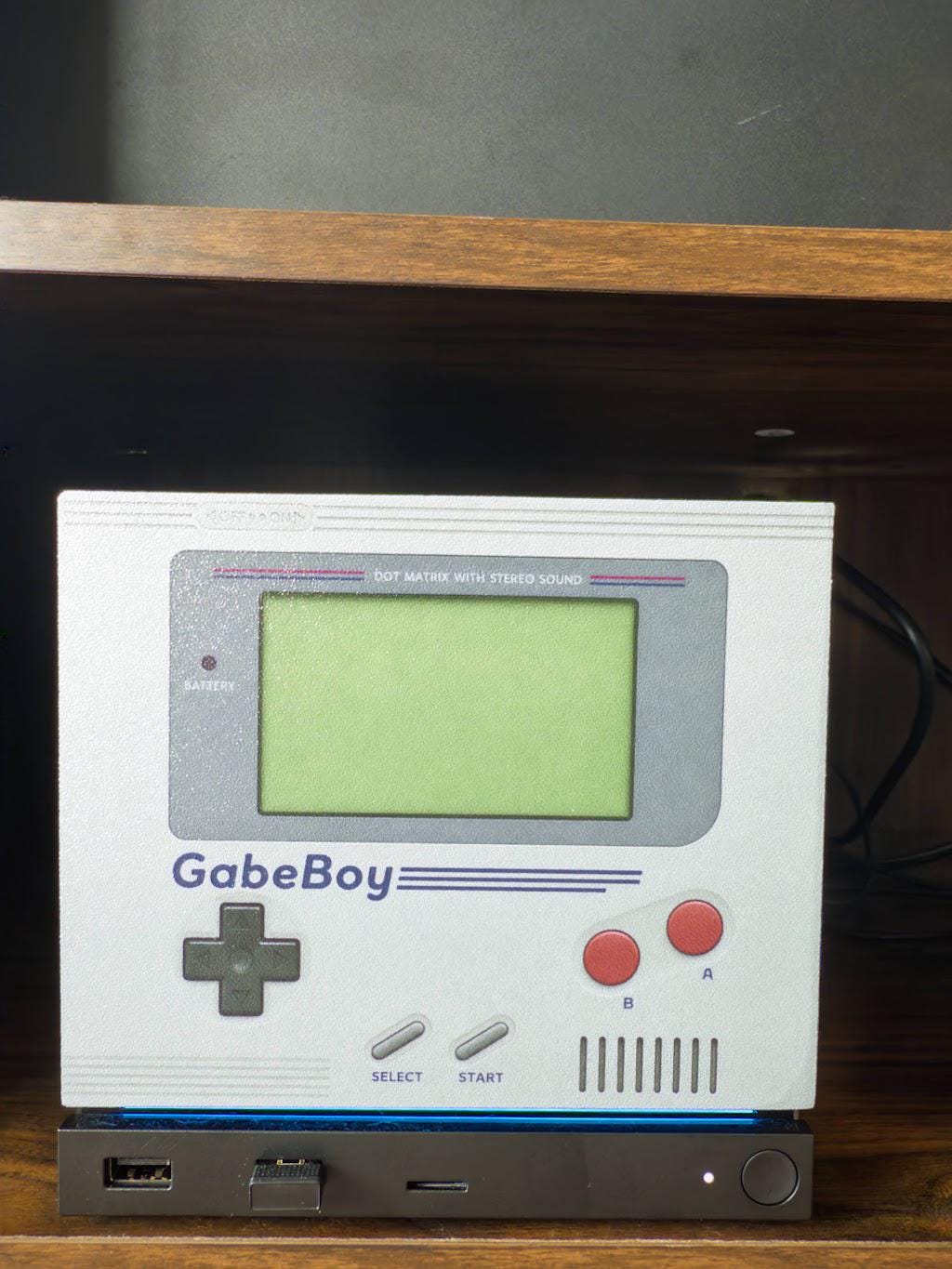 GabeBoy Retro Handheld Style Steam Machine Faceplate with green screen, D-pad and red buttons in retro handheld style, shown installed on the console sitting on a wooden shelf