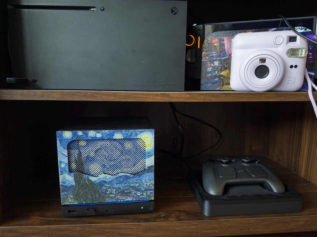 New Mesh!! Starry Night Steam Machine Faceplate Van Gogh Front Panel Fine Art UV Printed Magnetic Classic Painting Gamer Gift on the console on a wooden shelf next to a game controller, with a white instant camera and other electronics on the shelf above