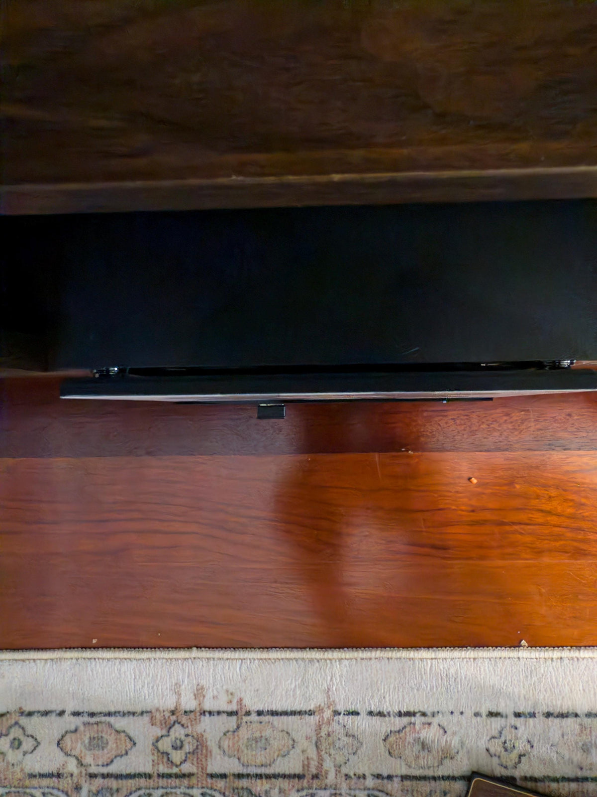 Retro Woodgrain Steam Machine Faceplate – 70s Atari Inspired Console Cover, dark photo of a flat-screen television on a polished wooden floor with a patterned rug visible at the bottom