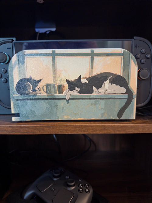 Custom 3D Printed Switch 2 Dock Faceplate, Magnetic Snap-On Cover (Personalized Photo), faceplate with an illustration of two cats resting on a windowsill shown installed on the Switch 2 dock on a wooden shelf, with a game controller on the shelf below