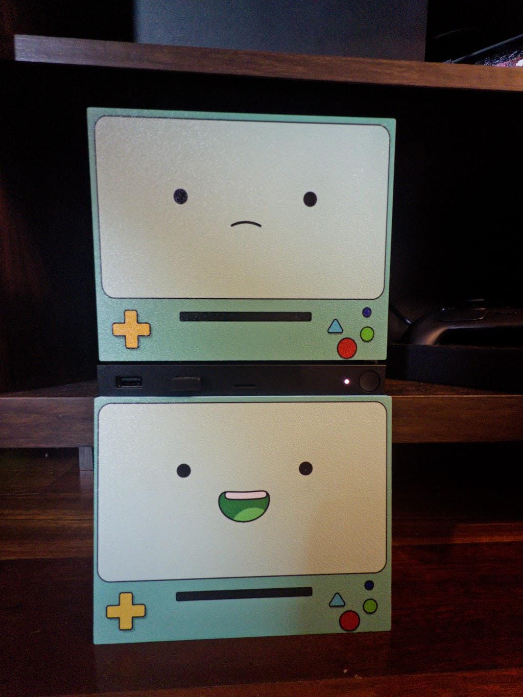 Robot Face Console Skin 2-Pack, Happy Sad Expression, Kawaii Gaming Setup Upgrade, with both skins stacked on a dark wooden shelf, the sad expression plate on top and the happy grinning plate below