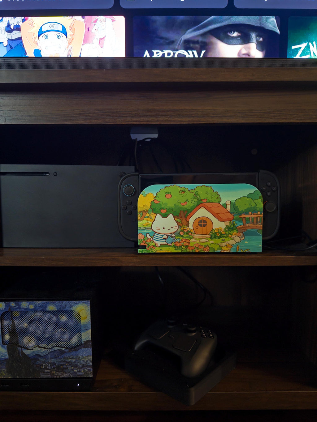 Custom 3D Printed Switch 2 Dock Faceplate, Magnetic Snap-On Cover (Personalized Photo), faceplate with a cute cottage and apple tree cartoon illustration shown installed on the Switch 2 dock on a wooden shelf next to an Xbox console, with a TV above