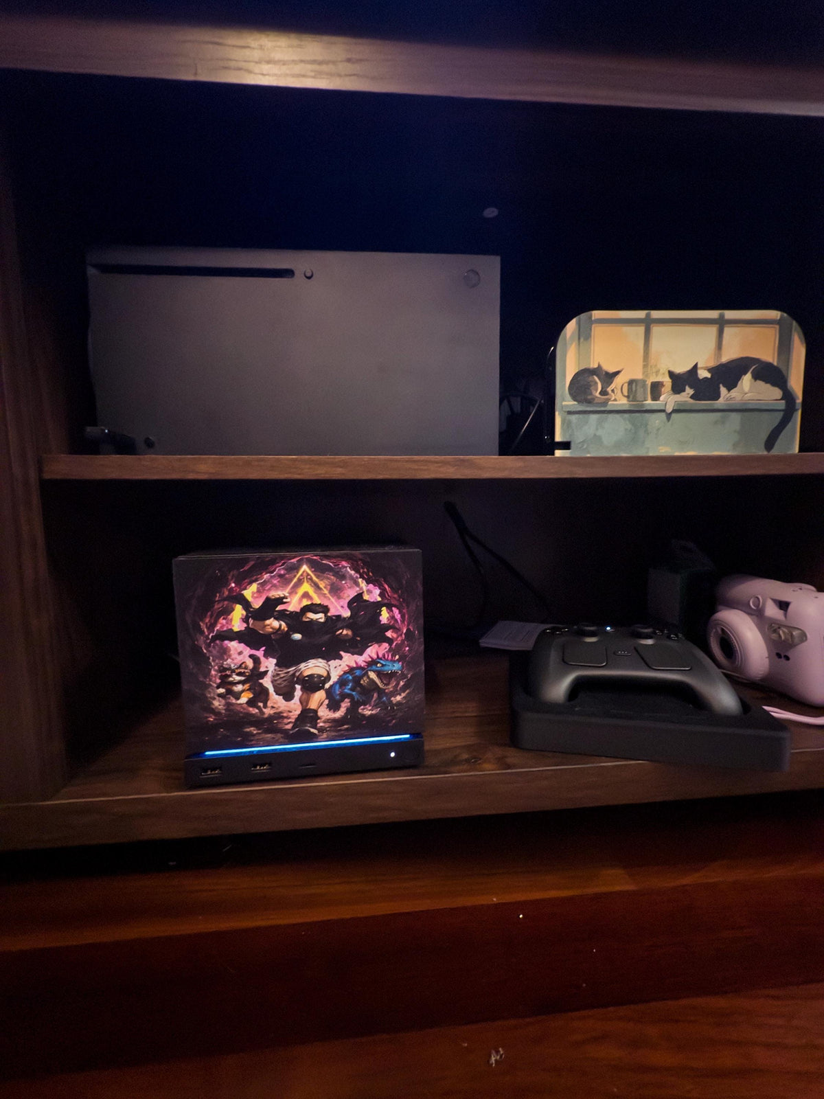 Dungeon Crawler Carl Steam Machine Faceplate | Licensed Landfin Studio Art (UV Printed) with Carl leaping through the glowing dungeon portal, shown installed on the console on a wooden shelf beside a game controller and a white instant camera, with a larger console on the shelf above