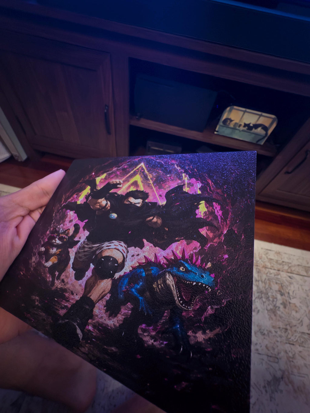 Dungeon Crawler Carl Steam Machine Faceplate | Licensed Landfin Studio Art (UV Printed) held in a hand, showing the printed panel front with Carl leaping through the glowing portal, tilted in front of a dark TV stand and television