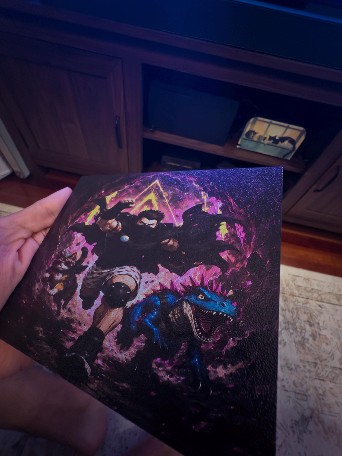 Dungeon Crawler Carl Steam Machine Faceplate | Licensed Landfin Studio Art (UV Printed) held in a hand, showing the printed panel front with Carl leaping through the glowing portal, tilted in front of a dark TV stand and television