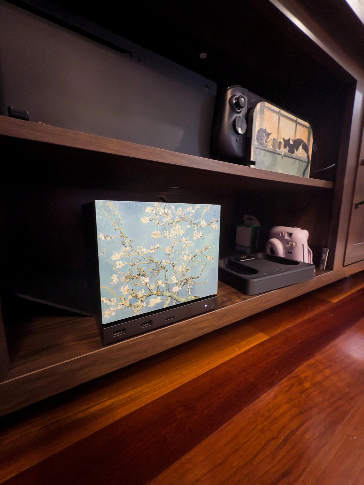 Van Gogh Almond Blossom Steam Machine Faceplate, Magnetic Art Cover Gaming Decor, side-angle view of the Steam Machine with the Almond Blossom faceplate installed on the lower shelf of a dark wooden unit, with a Steam Deck and Xbox on the shelf above