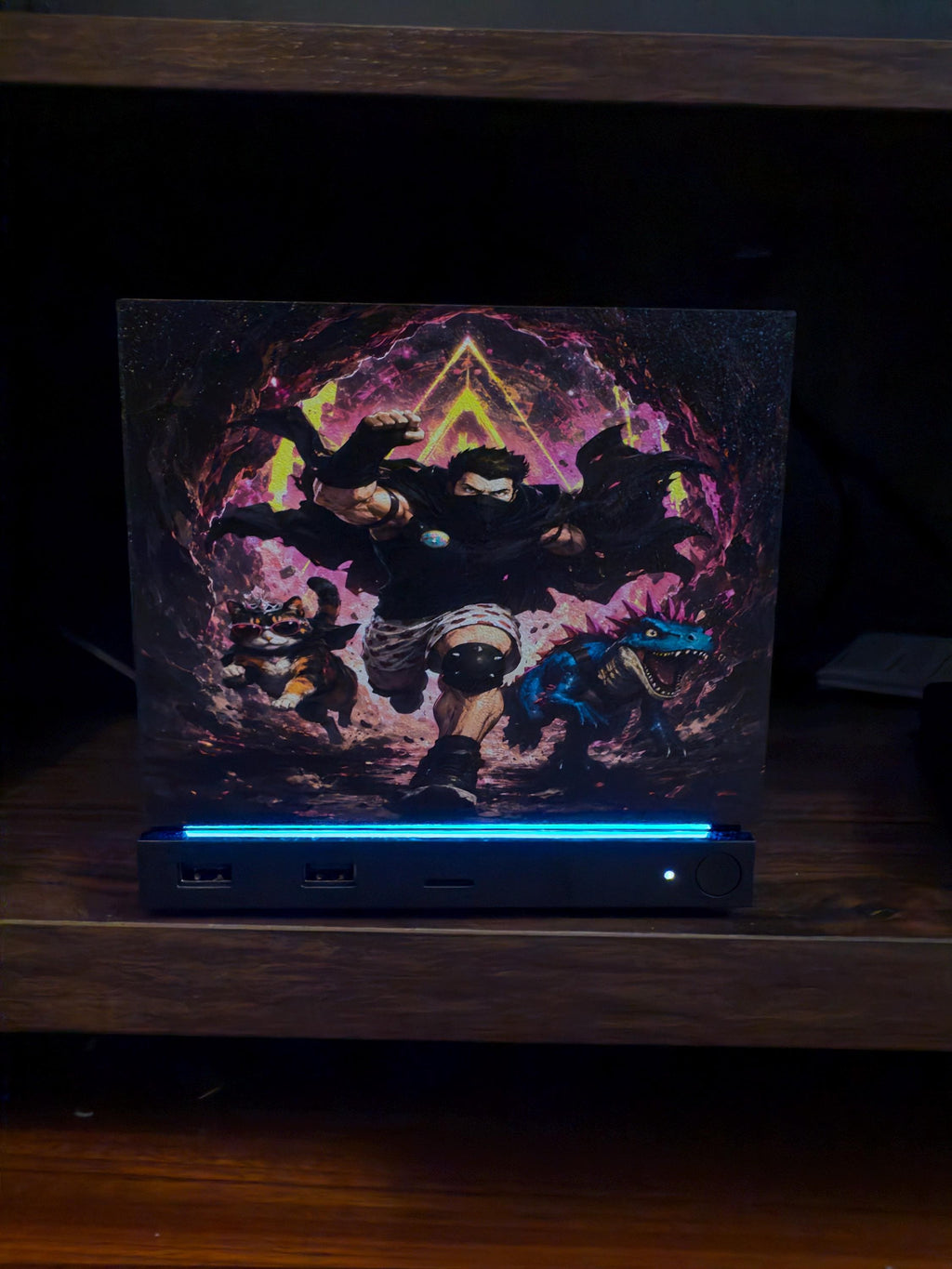 Dungeon Crawler Carl Steam Machine Faceplate | Licensed Landfin Studio Art (UV Printed) with Carl leaping through the glowing dungeon portal with Princess Donut and the blue creature, front view installed on the console on a dark wooden shelf with the blue LED strip glowing at its base