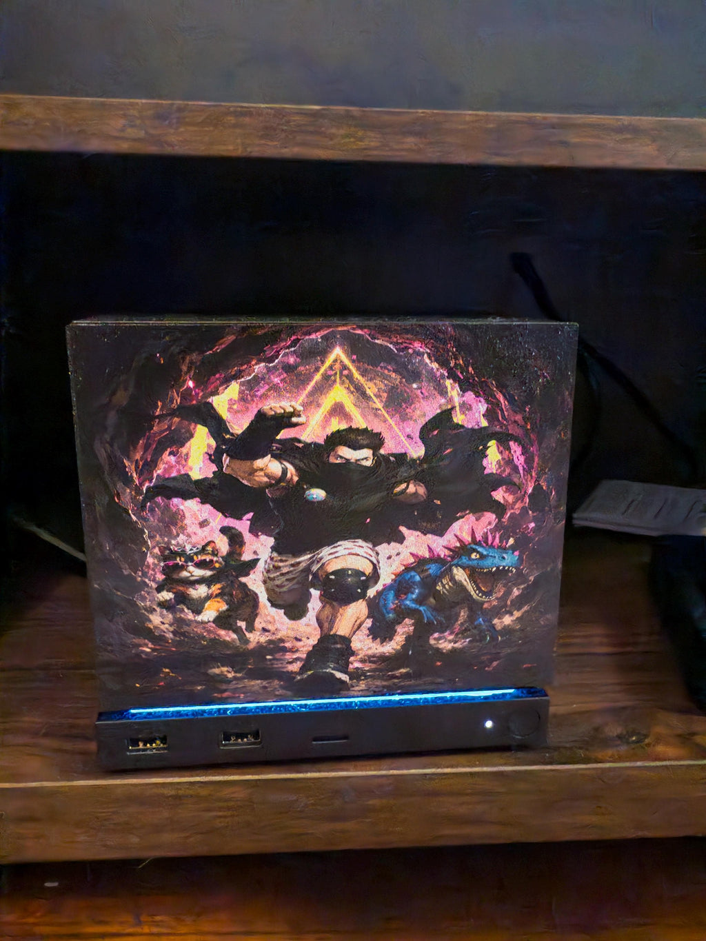 Dungeon Crawler Carl Steam Machine Faceplate | Licensed Landfin Studio Art (UV Printed) with Carl mid leap through the glowing dungeon portal with Princess Donut beside him, straight-on view installed on the console on a wooden shelf with a blue LED strip glowing at its base