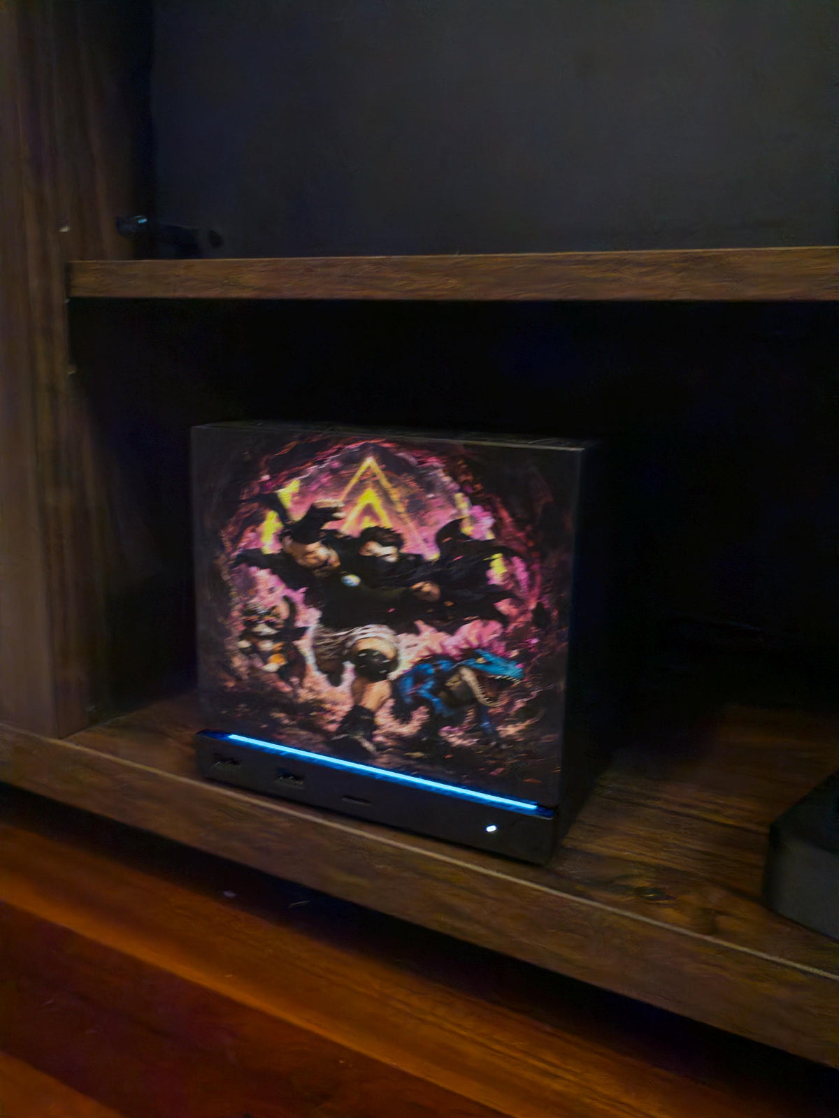 Dungeon Crawler Carl Steam Machine Faceplate | Licensed Landfin Studio Art (UV Printed) with Carl leaping through the glowing dungeon portal, angled close-up installed on the console inside a dark wooden shelf cubby with the blue LED strip glowing at its base