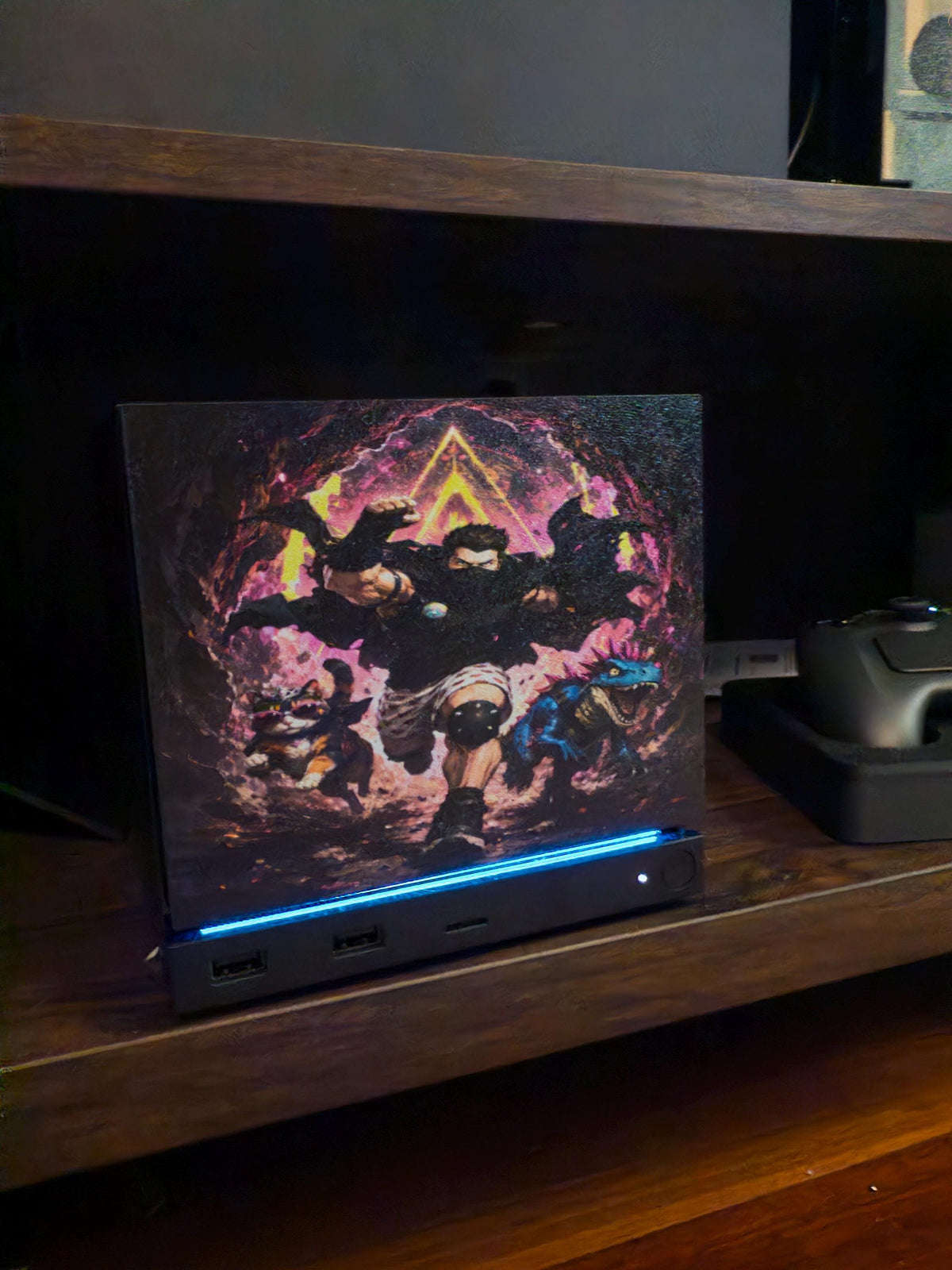 Dungeon Crawler Carl Steam Machine Faceplate | Licensed Landfin Studio Art (UV Printed) with Carl leaping through the glowing dungeon portal, three-quarter angle view installed on the console on a wooden shelf beside a game controller, with the blue LED strip glowing at its base