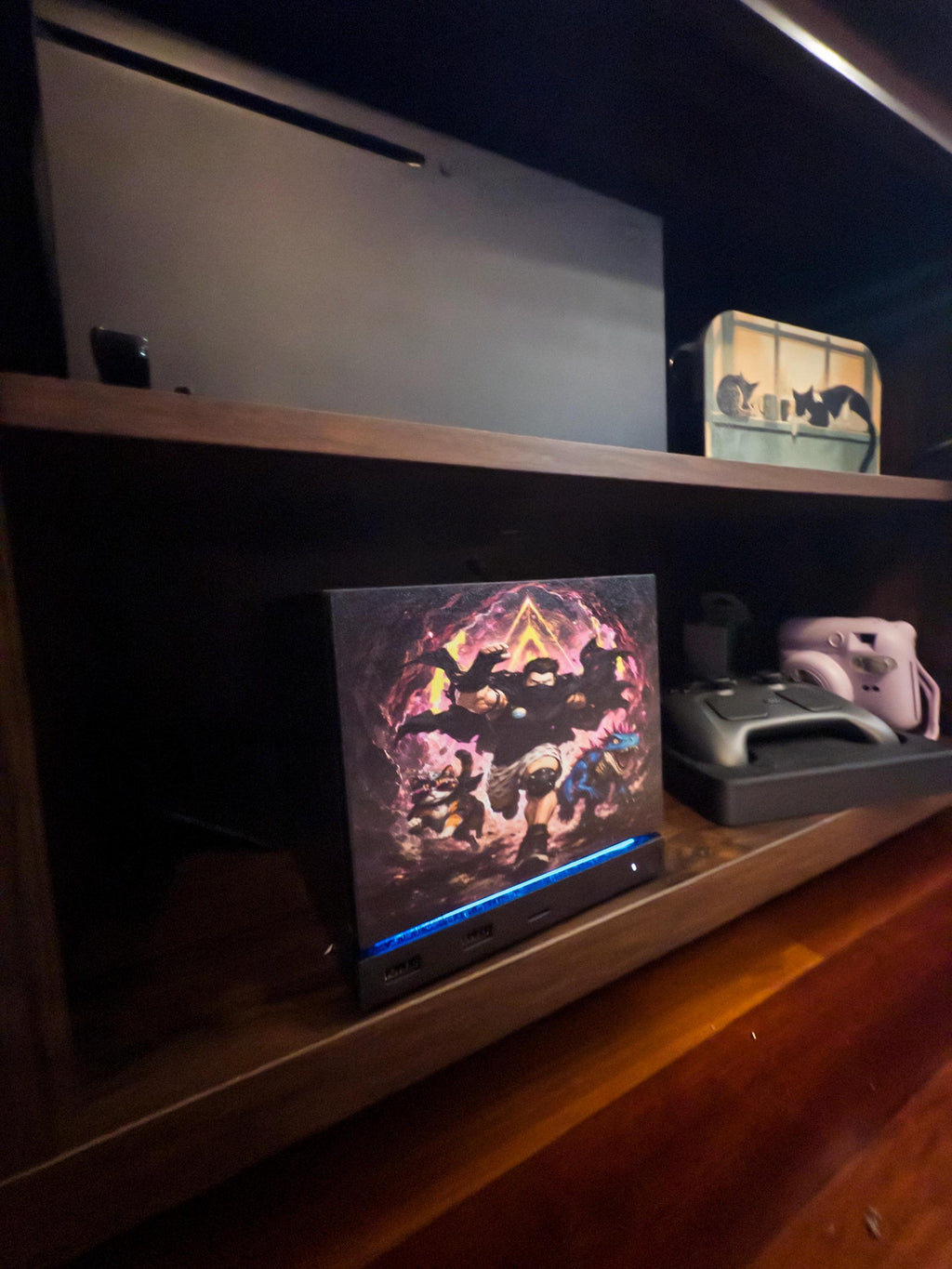 Dungeon Crawler Carl Steam Machine Faceplate | Licensed Landfin Studio Art (UV Printed) with Carl leaping through the glowing dungeon portal, angled view installed on the console on a wooden shelf beside a game controller and a white instant camera, with a larger console on the shelf above