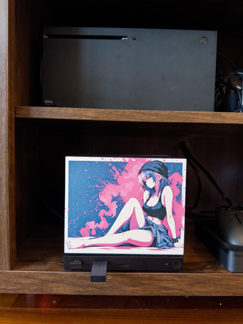 Anime Pinup Art Steam Machine Faceplate | Pink Blue Splatter Print | Magnetic UV Printed Panel | Stylish Gamer Gift with the pink and blue splatter anime girl art, close-up straight-on view of the faceplate installed on the console in a wooden shelf cubby with a game console on the shelf above