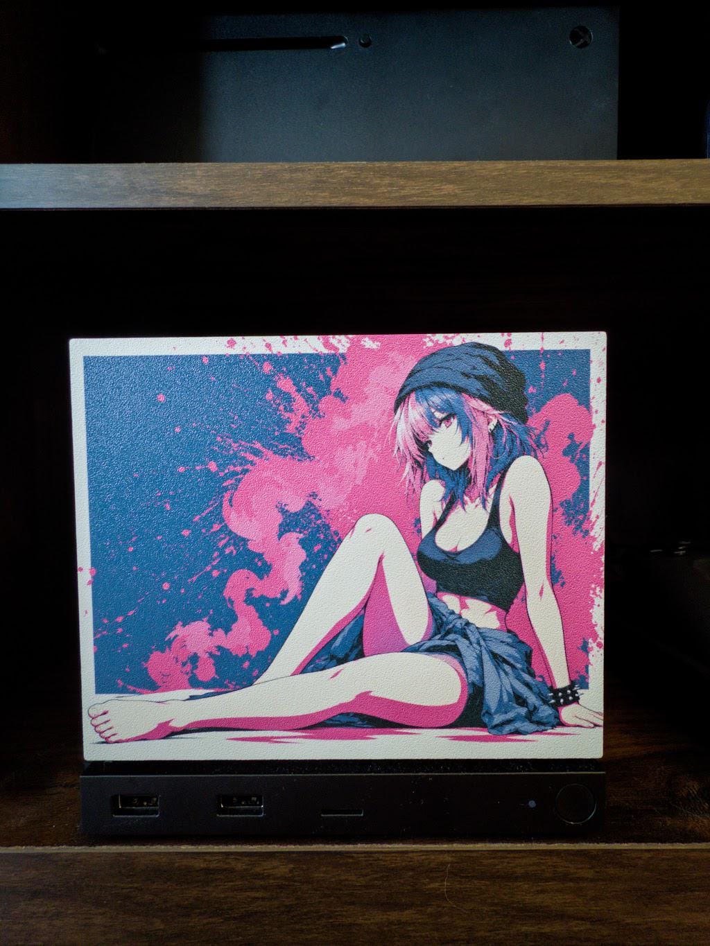 Anime Pinup Art Steam Machine Faceplate | Pink Blue Splatter Print | Magnetic UV Printed Panel | Stylish Gamer Gift with a relaxed anime girl in a black beanie and crop top against a pink and blue splatter background, shown installed on the console on a wooden shelf