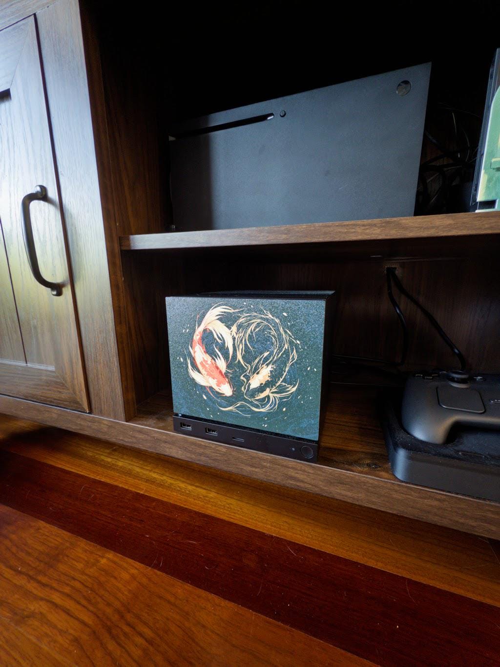 Koi Art Steam Machine Faceplate | Dark Teal Japanese Fish Panel | Magnetic UV Printed Cover | Zen Gamer Gift with two koi circling in dark teal water artwork, shown installed on the console in a wooden cabinet cubby beside a game controller