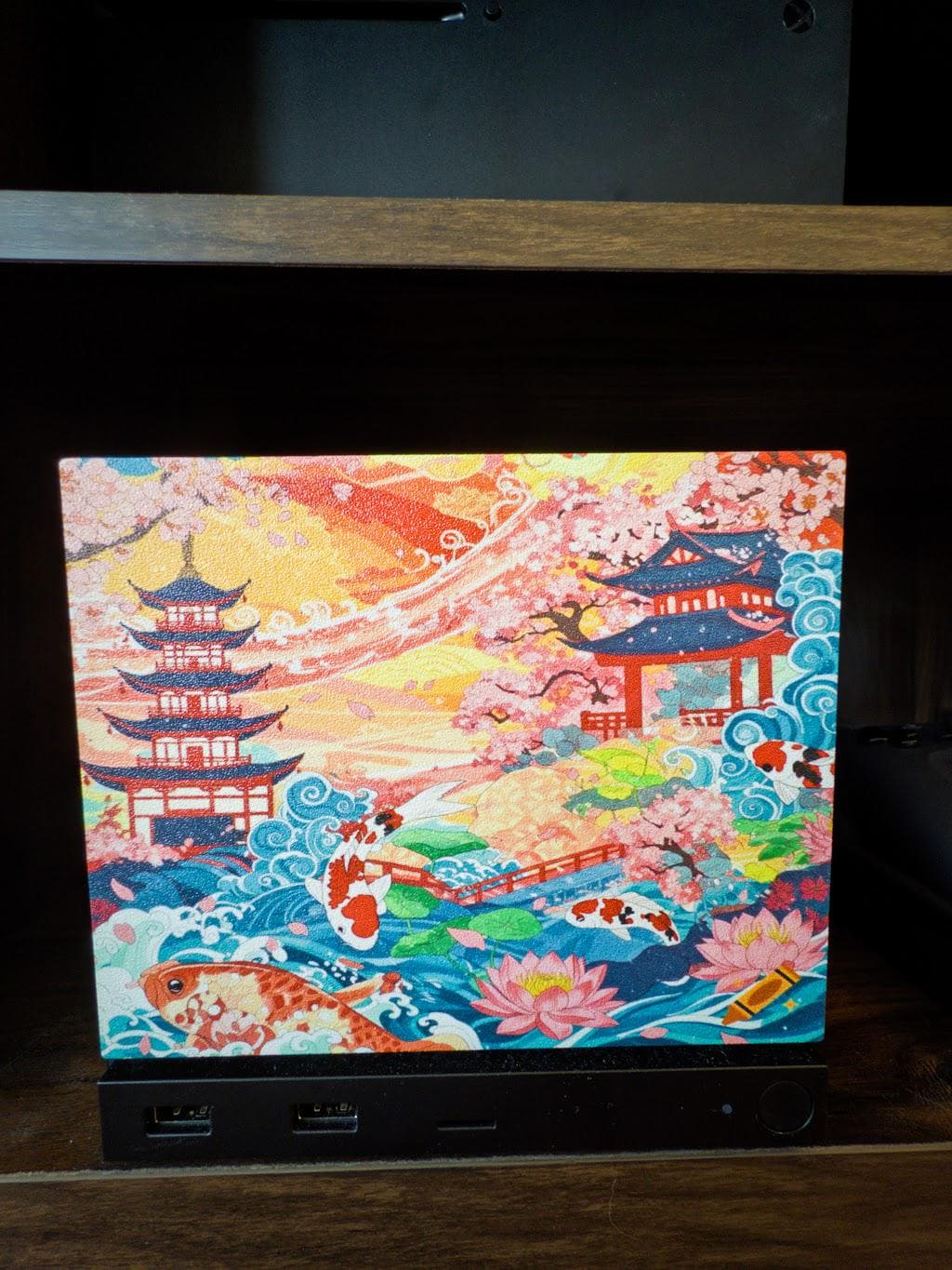 Koi Pagoda Garden Art | Steam Machine Faceplate | Cherry Blossom Sunset Panel | Magnetic UV Printed Cover | Japanese Gamer Gift with red and blue pagoda, cherry blossom, koi fish and lotus flower artwork, close-up straight-on view installed on the console on a wooden shelf