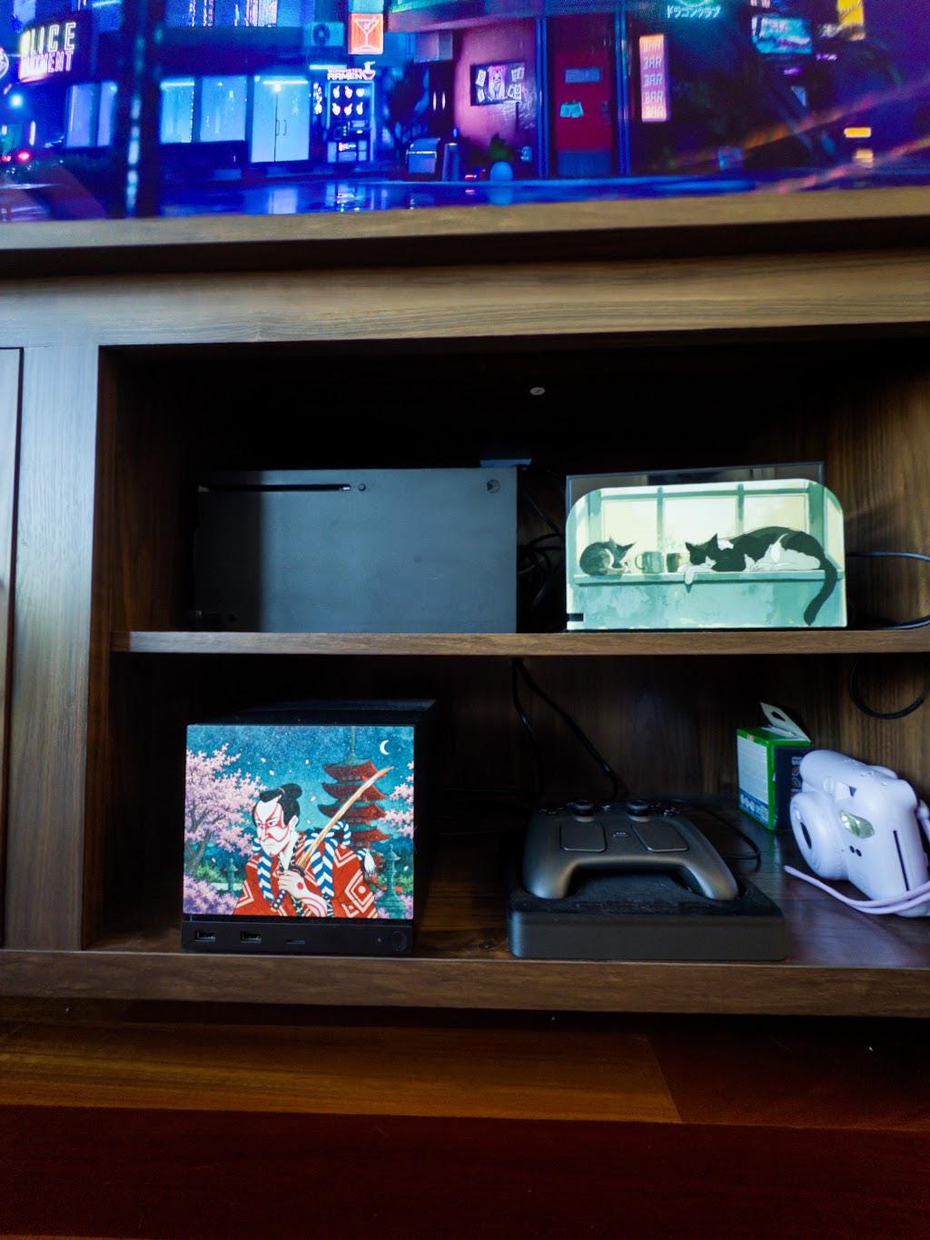 Kabuki Samurai Art Steam Machine Faceplate | Ukiyo-e Style Sword Panel | Magnetic UV Printed Cover | Japanese Gamer Gift with the kabuki actor artwork, visible on the console in the lower shelf of a wooden media console beneath a large TV showing a neon cityscape, beside a game controller and a white instant camera