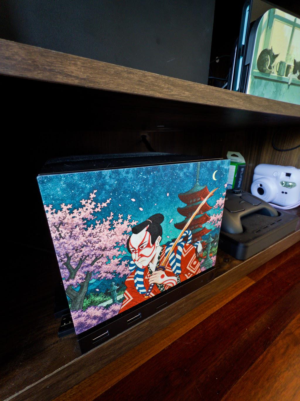 Kabuki Samurai Art Steam Machine Faceplate | Ukiyo-e Style Sword Panel | Magnetic UV Printed Cover | Japanese Gamer Gift with the kabuki actor artwork, three-quarter angle view installed on the console on a wooden shelf beside a white instant camera and a game controller