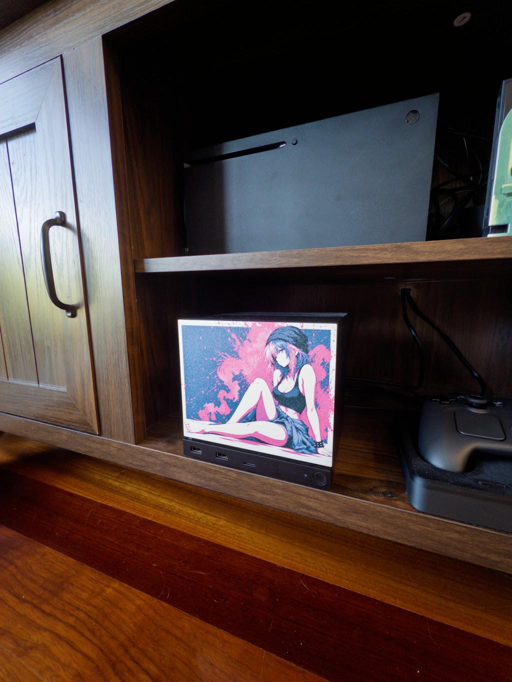 Anime Pinup Art Steam Machine Faceplate | Pink Blue Splatter Print | Magnetic UV Printed Panel | Stylish Gamer Gift with the pink and blue splatter anime girl art, side view of the faceplate installed on the console in a wooden cabinet cubby with a larger console on the shelf above and a game controller below