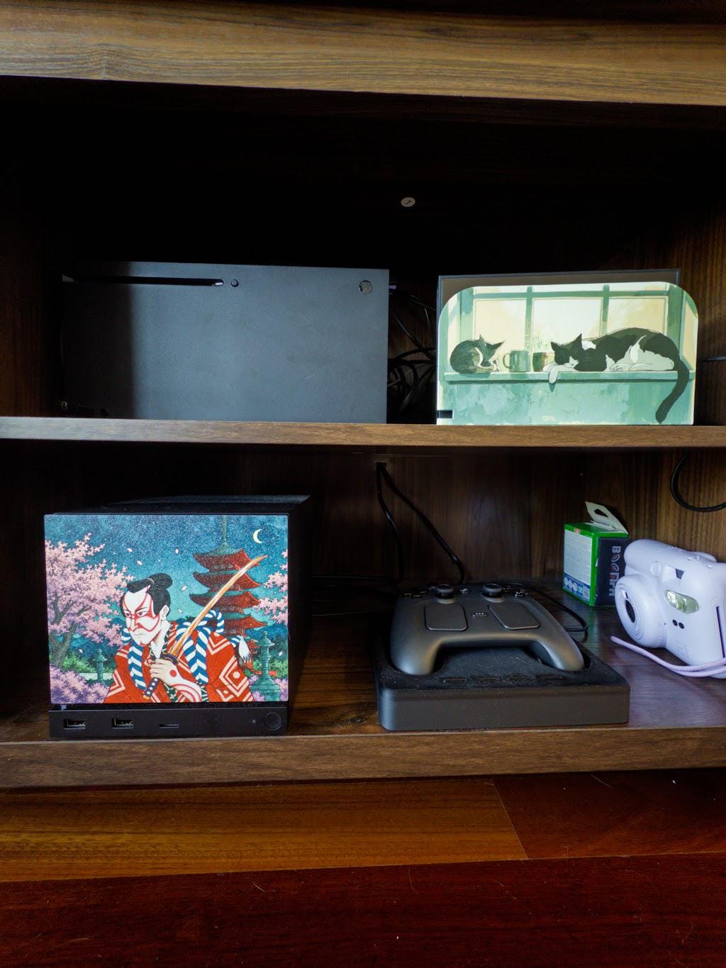 Kabuki Samurai Art Steam Machine Faceplate | Ukiyo-e Style Sword Panel | Magnetic UV Printed Cover | Japanese Gamer Gift with the kabuki actor artwork, installed on the console in a wooden shelf cubby beside a game controller and a white instant camera, with a cat picture frame on the shelf above