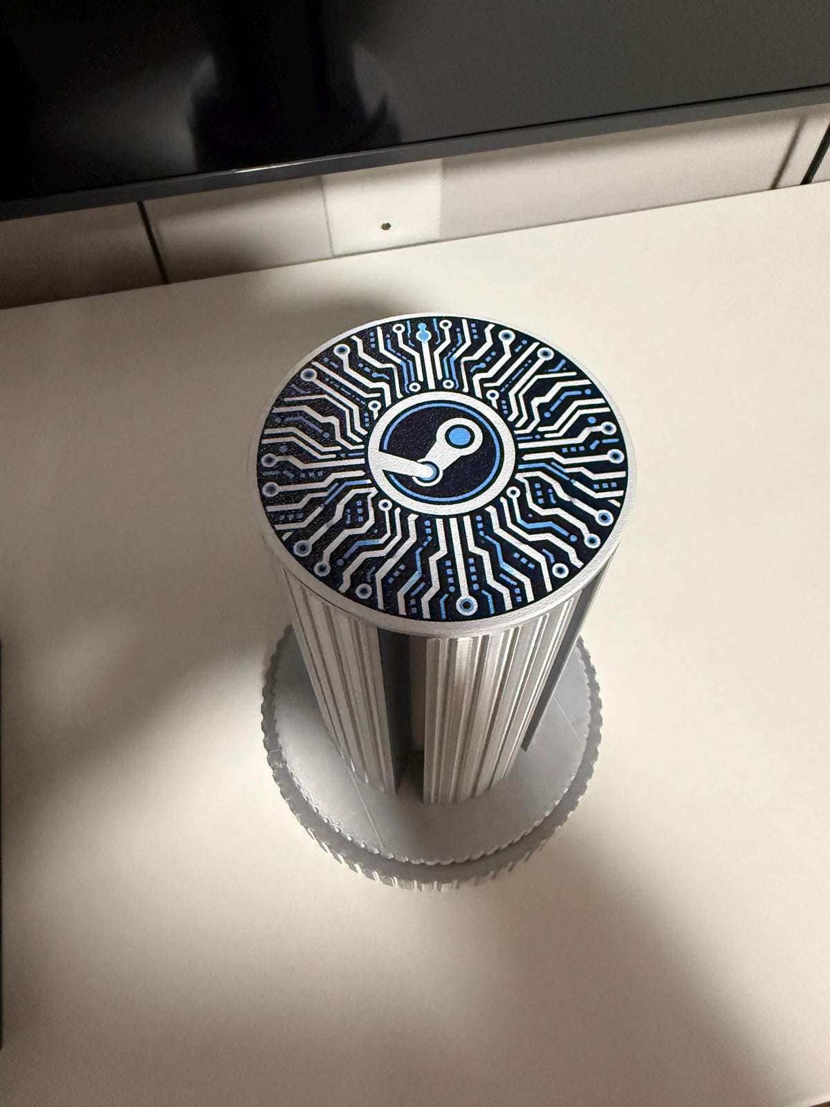 Steam Machine Faceplate Organizer, Spinning 3D Printed Display Stand, Rotating Plate Holder, Gamer Desk Setup, Gift for Gamer, Holds 6, top-down view of the empty organizer column with the circuit-board Steam logo top cap on a white desk beneath a monitor