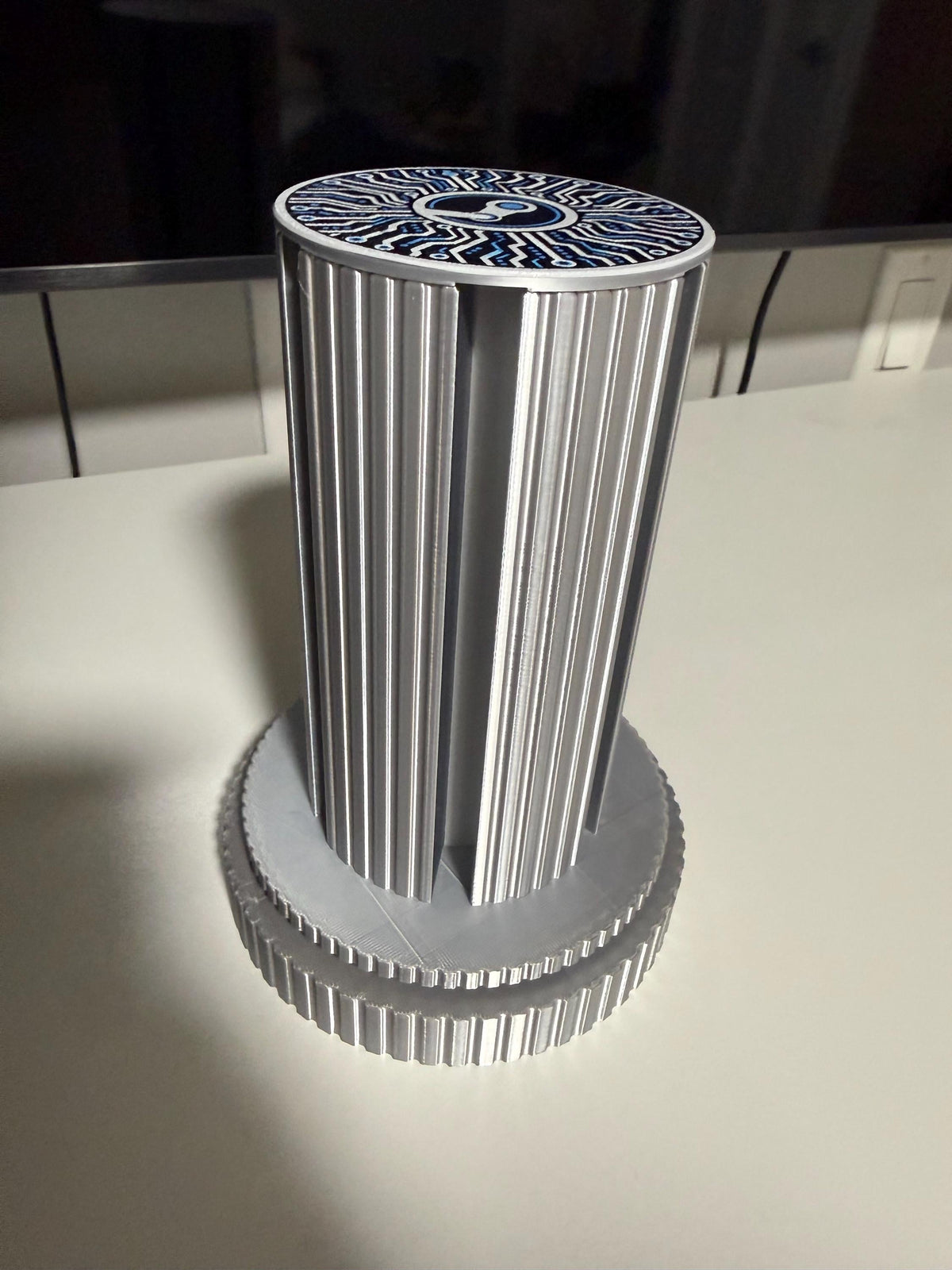 Steam Machine Faceplate Organizer, Spinning 3D Printed Display Stand, Rotating Plate Holder, Gamer Desk Setup, Gift for Gamer, Holds 6, angled view of the empty silk silver organizer column standing alone on a white desk in front of a TV, showing the circuit-board patterned top cap
