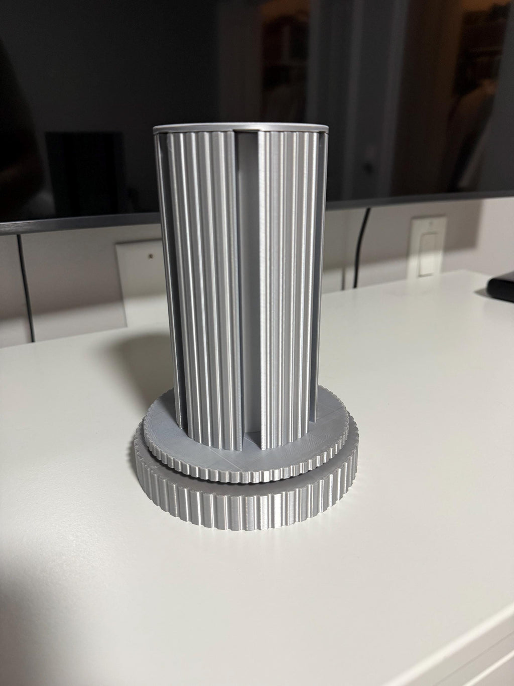 Steam Machine Faceplate Organizer, Spinning 3D Printed Display Stand, Rotating Plate Holder, Gamer Desk Setup, Gift for Gamer, Holds 6, straight-on eye-level view of the empty silk silver organizer column standing alone on a white desk with a dark monitor behind, showing the fluted column and ridged circular base