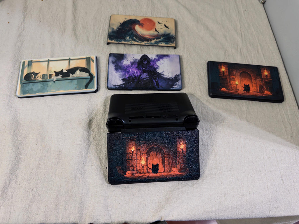 AYN Thor Custom Lid, HD Full Color UV Printed Snap On Cover, Personalized Handheld Faceplate, Your Own Image, Interchangeable Shell, five lids on a light fabric surface with one dungeon door lid installed on the closed handheld, alongside uninstalled wave, hooded figure, window cats, and second dungeon door lids