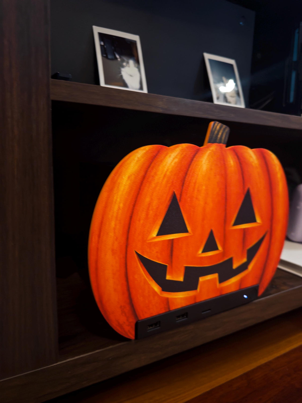 Steam Machine Faceplate Halloween Pumpkin, Classic or Cute Jack o Lantern Magnetic Plate, UV Printed Console Cover, Spooky Gamer Gif, angled view of the classic carved jack-o-lantern pumpkin faceplate installed on the Steam Machine on a dark wooden shelf, with two framed cat photos on the shelf above