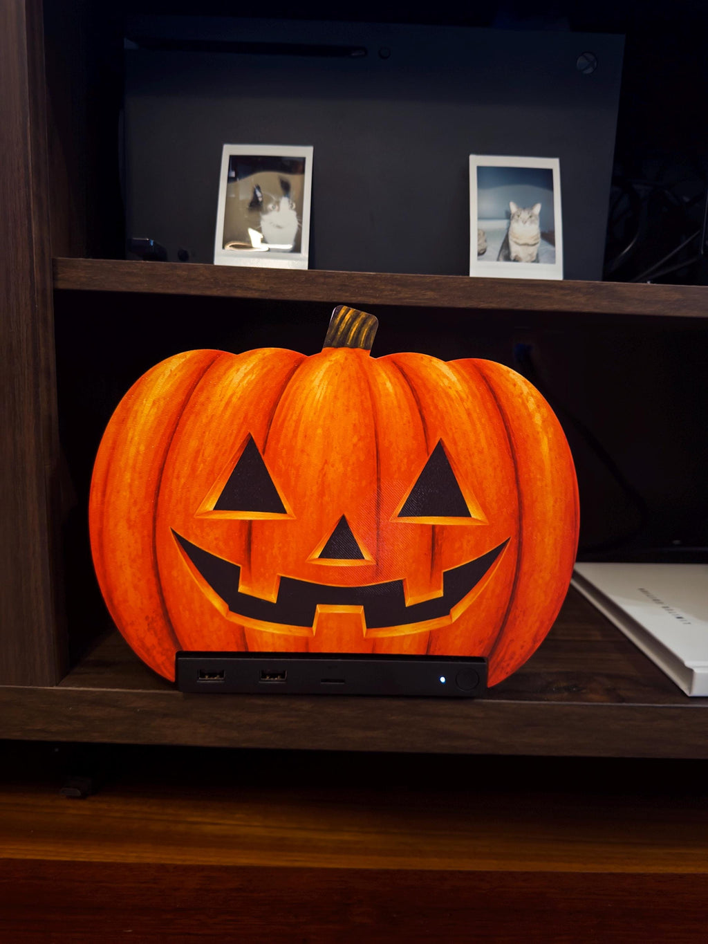 Steam Machine Faceplate Halloween Pumpkin, Classic or Cute Jack o Lantern Magnetic Plate, UV Printed Console Cover, Spooky Gamer Gif, classic carved jack-o-lantern pumpkin faceplate installed on the Steam Machine on a wooden shelf, with a white book beside it and two framed cat photos on the shelf above